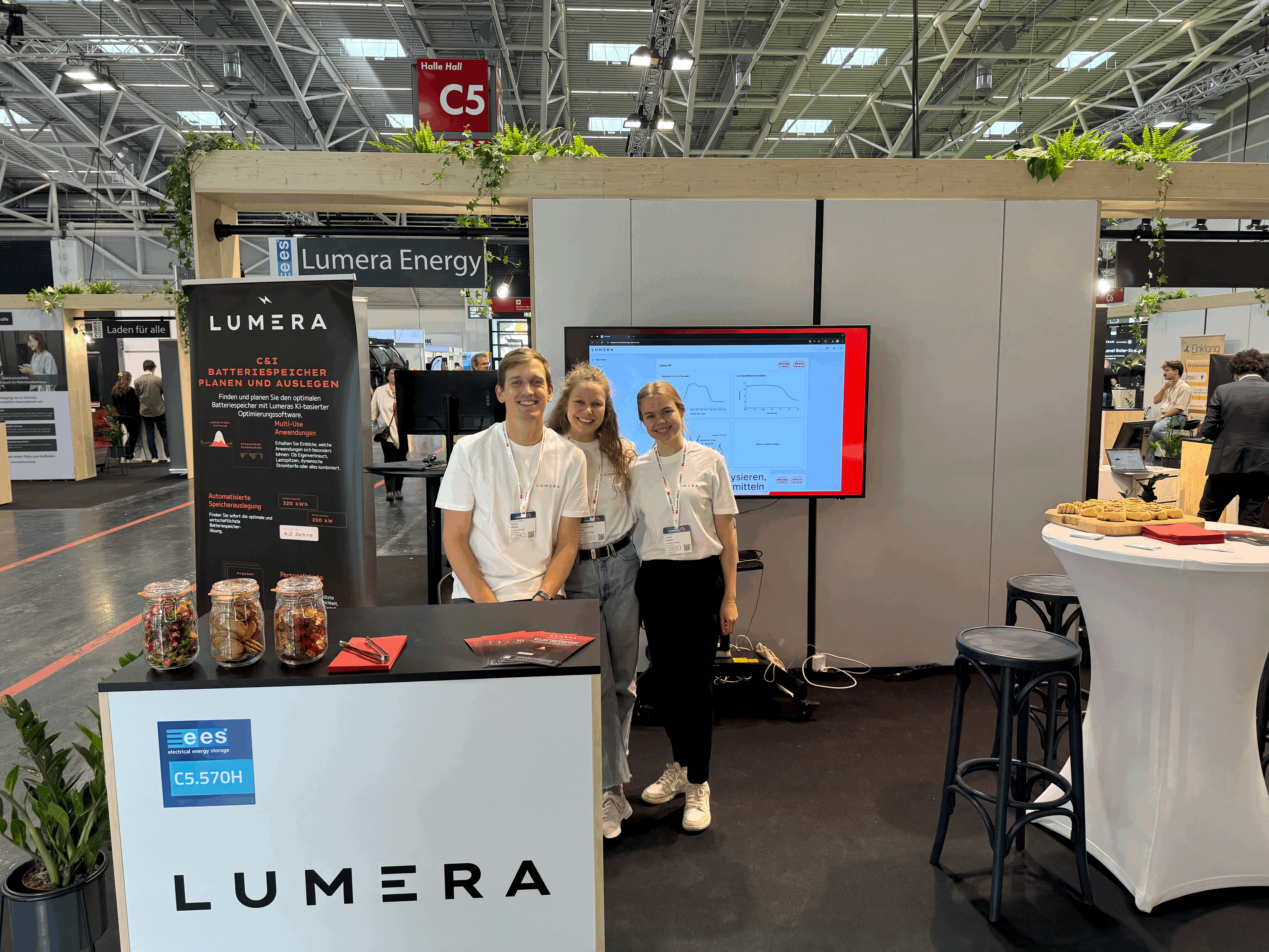 Drei Personen am Lumera-Energy-Messestand mit Software-Dashboard auf dem Bildschirm