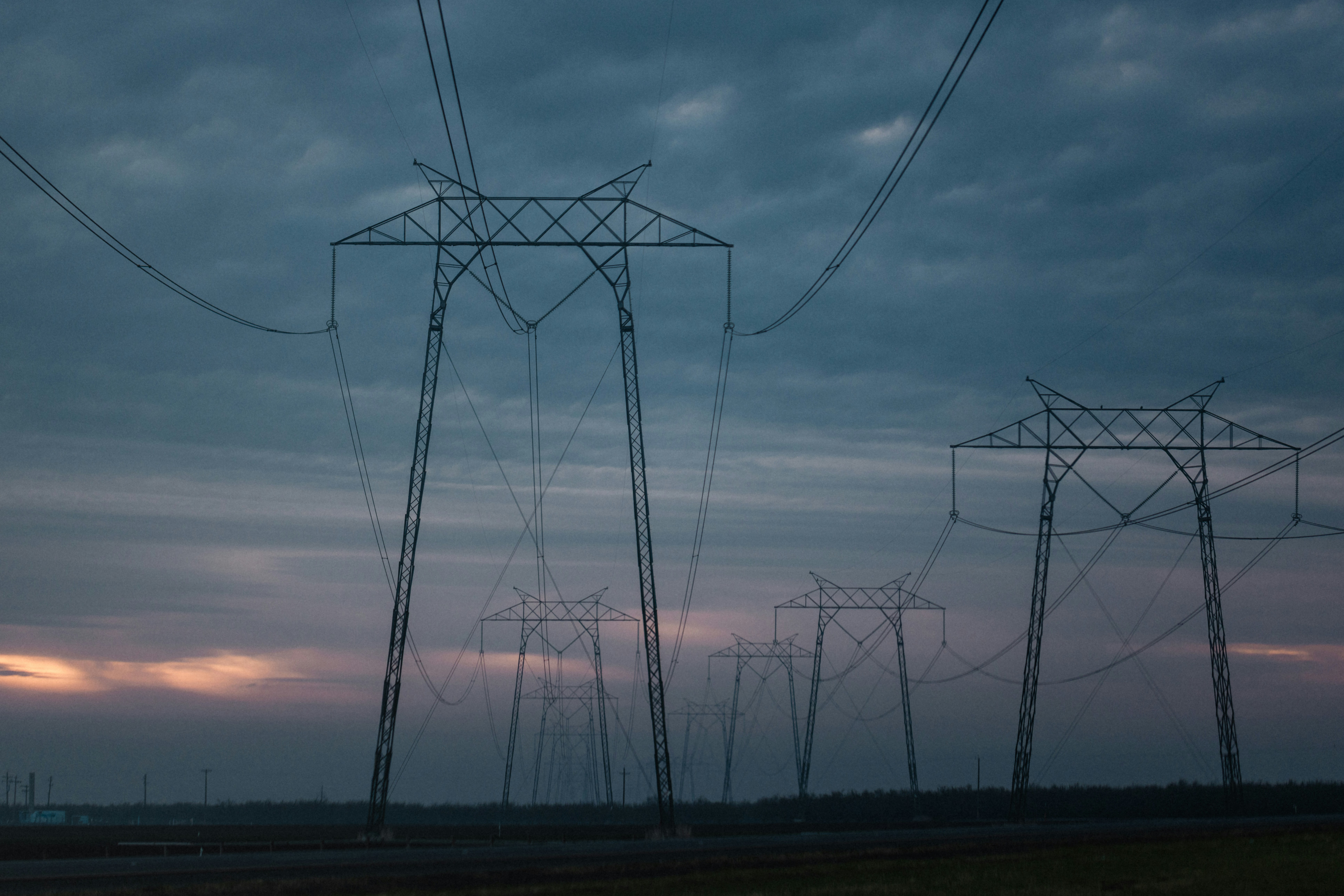 Hochspannungsmasten mit Stromleitungen vor dunklem Abendhimmel in einer Landschaft